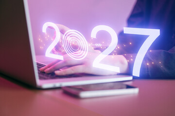 Working on a laptop with a display showing the year 2027 and a target symbol over a desk space during an evening setting