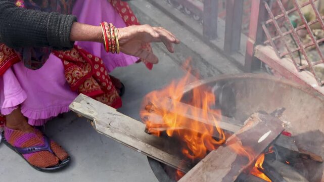 An Indian village woman warms her hands near an open fire, showing winter cold, traditional lifestyle, and everyday rural life practices in an Indian village setting.