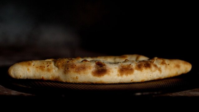Traditional georgian cheese-filled bread, megruli khachapuri, rotating on a wooden board against a black background. Appetizing golden-brown crust