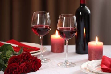 Beautiful table setting with glasses of wine, burning candles and red roses indoors, closeup