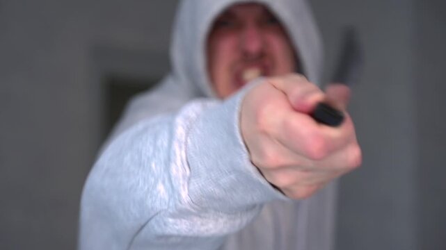 A hooded hooligan threatens someone with a knife.
The person attacks with a knife.
A sharp knife in the hands of an aggressive man.