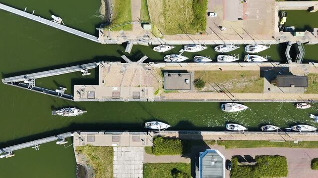 numerous white sailboats neatly queued transitioning through concrete industrial channels perspective narrow maritime locks along afsluitdijk netherlands top down 