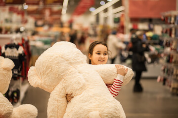 A young girl hugging a large white teddy bear in a store, wearing a red and white striped sweater,...