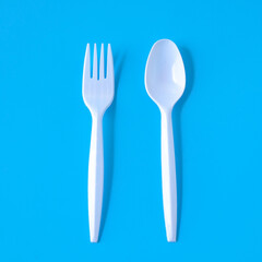 white plastic fork and spoon on color background.