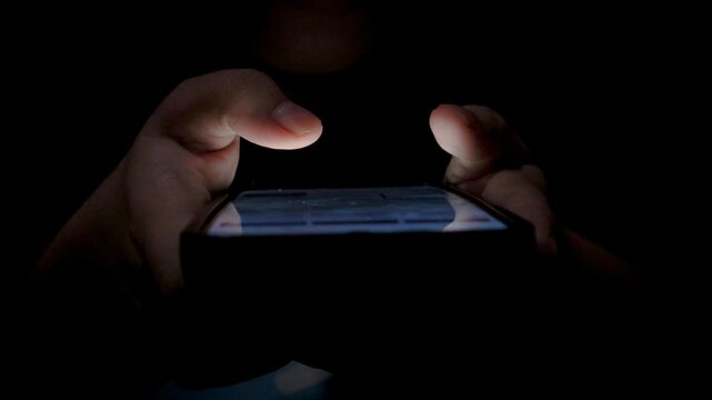 Close-up of a woman using a smartphone in a dark bedroom, browsing the internet and scrolling the screen with her finger. Close-up of a female hand scrolling on a mobile phone in a dimly lit room. 