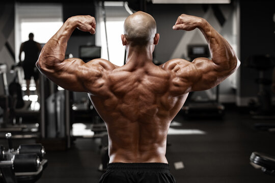 Muscular man showing back muscles in gym. Strong male rear view