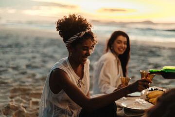 Friends enjoying a beach picnic with drinks during a beautiful sunset