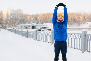 Man extending arms overhead, stretching body for exercise. Staying active and healthy during winter season