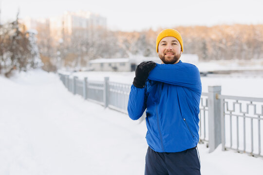 Man stretching arm in winter park, preparing for outdoor running or fitness exercise in snow