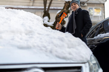 Man holding snow brush clearing snow from car