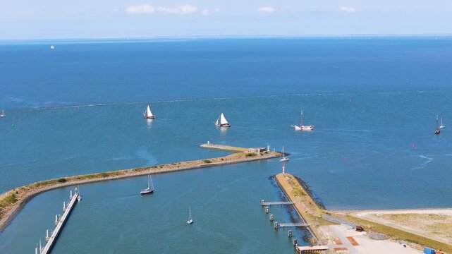 traditional modern sailboats cruise through narrow harbor entrance defined by stone breakwaters path leads into vast shimmering blue wadden sea afsluitdijk netherlands water 