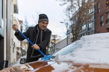 Man clearing snow from car windshield on winter day