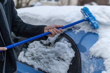 Person clearing snow from blue car roof