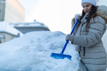 Woman clearing accumulating snow from frosted car