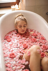 Serene woman relaxing in rose petal bath with candles lit nearby