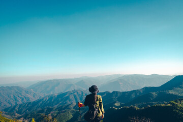 Obraz premium A woman in hiking gear walking on a high ridge. She carries a large backpack and holds trekking poles. There is a view of the mountains in layers and bright light. Idea for adventure wallpaper.