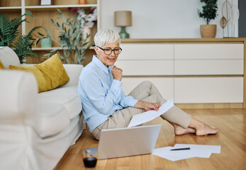 Portrait of a senior woman working on laptop sitting on the floor at home