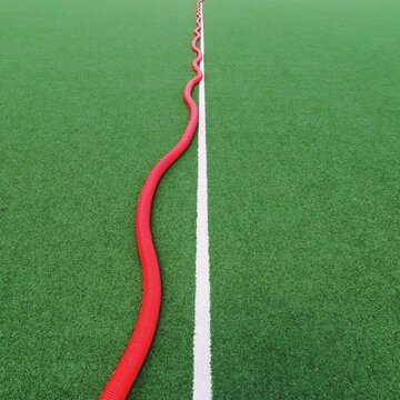 Full frame close-up of a Single white line on a green sports field with a red hosepipe alongside
