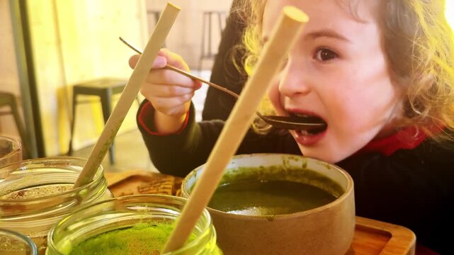 Child eating green soup with bread at cafe table
