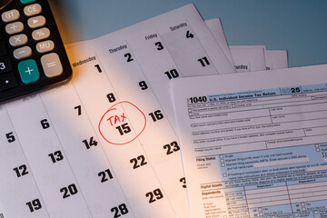 April 15 Tax Day marked with a red circle on a white calendar next to IRS Form 1040 and blue glasses in soft window light on table.