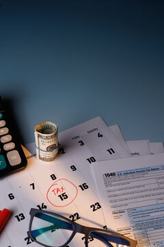 Tax Day deadline with a red circle on 15 and IRS Form 1040 in color near blue glasses and a calculator in warm solar light on table.