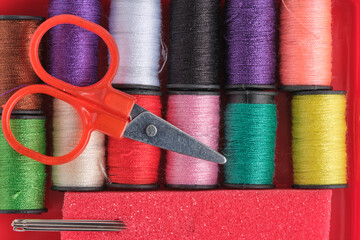 Colorful spools of thread, scissors and needle on red background.