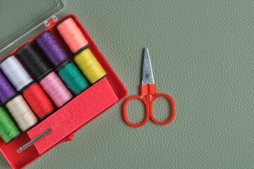 Sewing supplies spools thread, needles and scissors in red box on green background, top view.