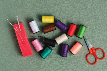 Spools of thread, scissors and needle on green background.