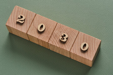 Wooden cubes with year 2030 on green background, business concept.