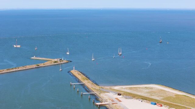 several white sailboats navigate through harbor entrance flanked by stone breakwaters head out into vast bright blue waters under clear sky afsluitdijk netherlands long nautical navigation 
