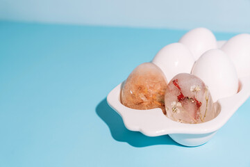 Minimal egg carton with eggs and frozen floral ice egg on pastel blue background. High quality photo