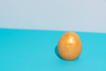 Single gold silicone egg on blue background, minimal Easter concept. High quality photo