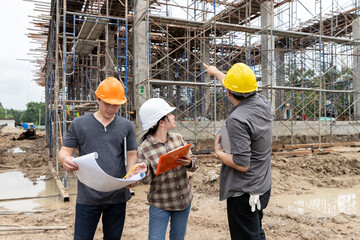 Team of civil engineers and architects discussing construction plan with blueprint and pointing at scaffolding structure.