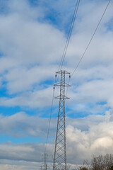 A high-voltage transmission tower rising under a blue sky and white clouds. Energy transmission and industrial infrastructure concept.