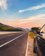 Scenic road trip at sunset with car parked on the roadside. Empty asphalt highway into the distance...