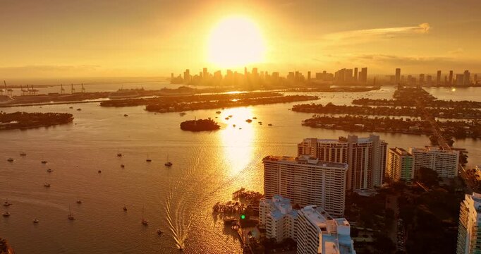 Golden hour over the stunning Biscayne Bay. Flight over the waterscape with numerous vessels on. Approaching the skyline silhouette of Miami, Florida, USA.
