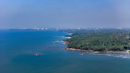 Fototapeta premium Breathtaking aerial view of the Kerala shoreline, showcasing a dense forest of coconut trees bordering the waves of the Indian Ocean and kannur city