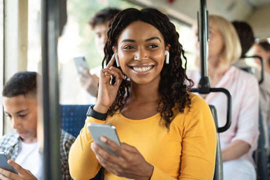 Urban Lifestyle. Smiling African American woman on train listening to music on smartphone. Young lady using cell phone app and wireless headphones to listen to audiobook, enjoying travel