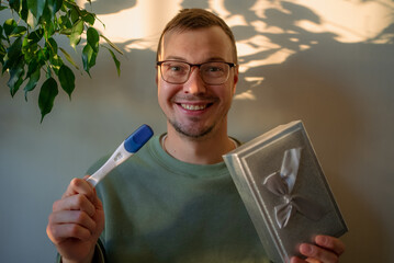 Happy man celebrating a positive pregnancy test result and holding a gift, expressing joy and surprise about becoming a future father and expecting a baby