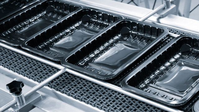 A conveyor belt with open plastic containers for packaging food products in a food production and packaging plant or factory.