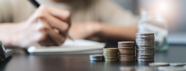 Close up stack of coins on the table and woman do accounting as background