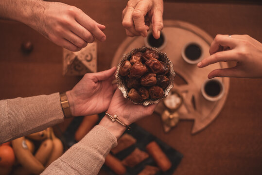 Hands Sharing Dates During Ramadan Celebration Close-Up Top View of Generational Family Members Enjoying Traditional Food Together During Iftar Meal at Home.