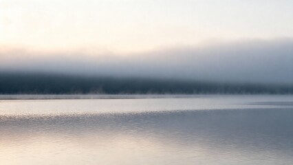 Fototapeta premium Soft fog rises from the calm waters of a lake during early morning hours. Gentle hues of light create a magical and serene scene that invites peaceful thoughts.
