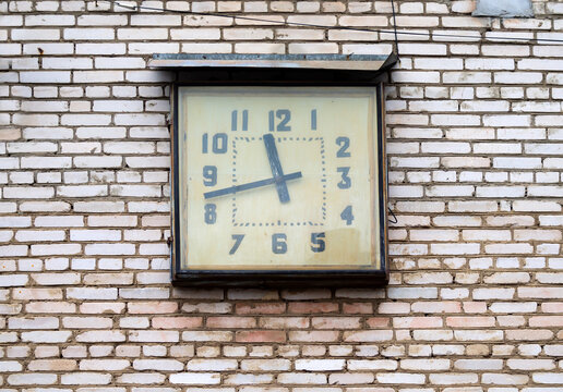 A square factory clock on the wall of a workshop building. Soviet era.