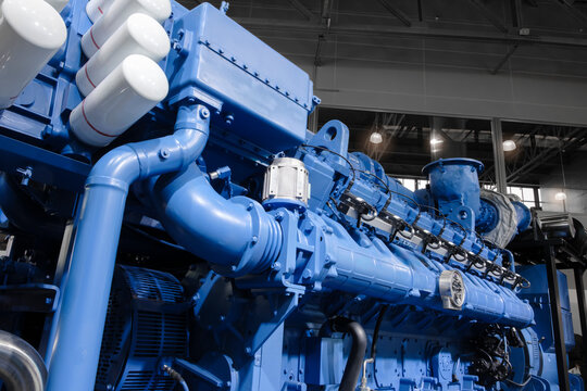 Large  piston gas engine electric generator with many valves and pipes. The engine is orange and has many valves.