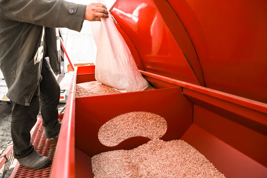 Farmer pouring grain from a sack into a tractor seed drill. High quality photo