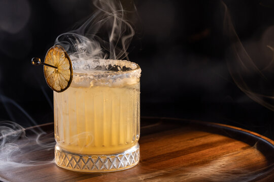Refreshing smokey margarita with salt on the rim served on ice garnished with a grilled lime wheel.