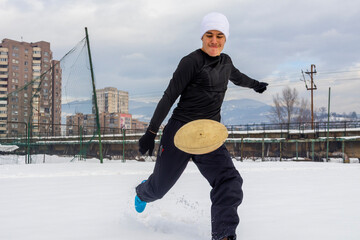 Athletic man kicking a rugby ball on a snow covered urban sports field, captured mid action during...