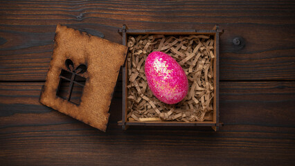 Glittering Pink Egg in Decorative Wooden Box with Shredded Fill on Rustic Wooden Background