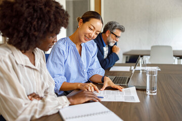 Obraz premium Female lawyers reviewing legal documents and discussing strategies while male colleague works in background in modern office